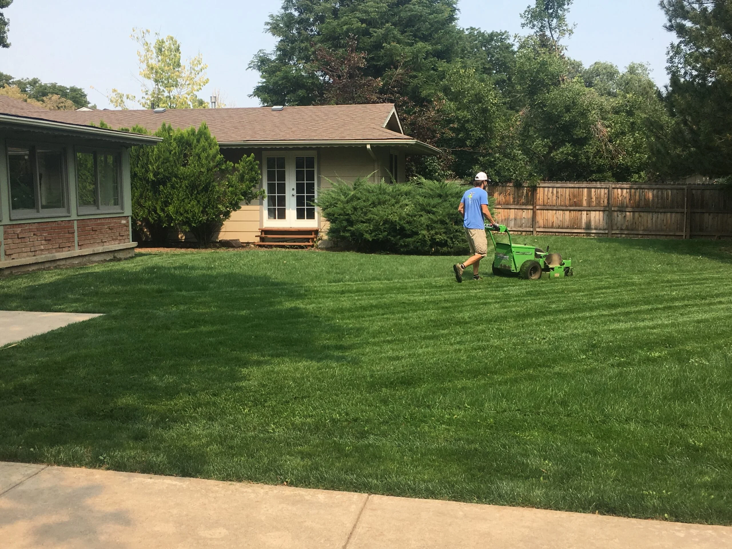 Lawn care professional mowing a large green residential yard